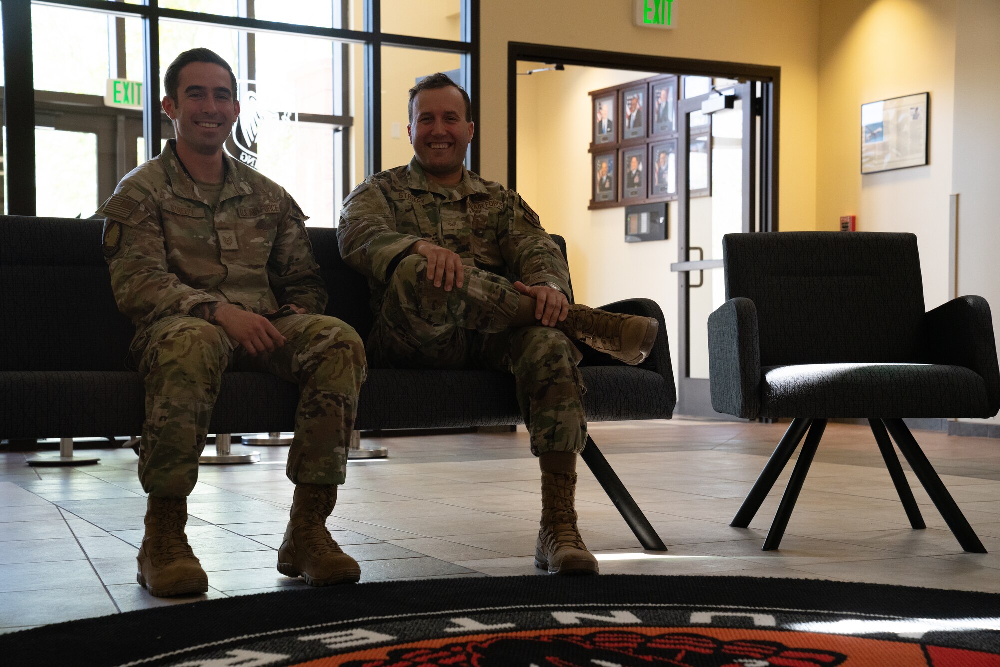 Two men in military uniforms sit on a couch smiling.