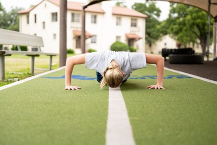 woman does pushup on turf outside in the bright sunlight