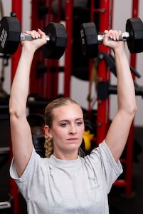 woman lifts weights above her head in the gym
