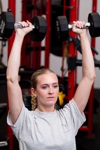 woman lifts weights above her head in the gym
