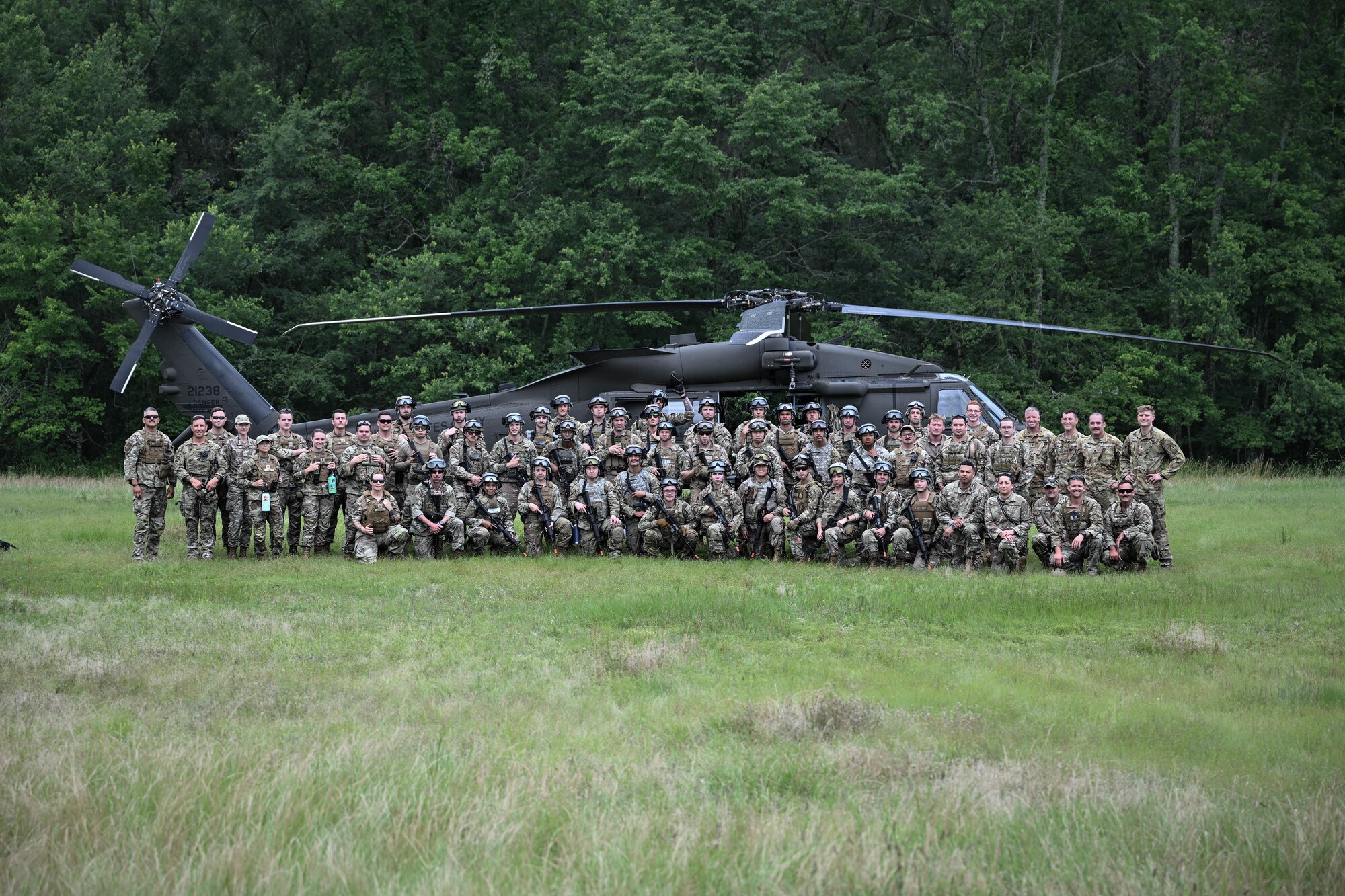 Airmen and Soldiers pose for a photo in front of a helicopter in a grass field.