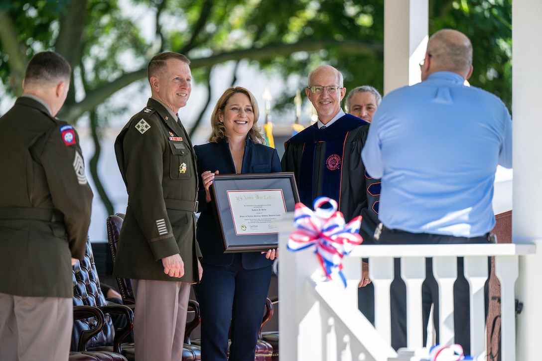 Deputy Defense Secretary Kathleen Hicks stands for a photo with a service member and holds up a framed certificate.
