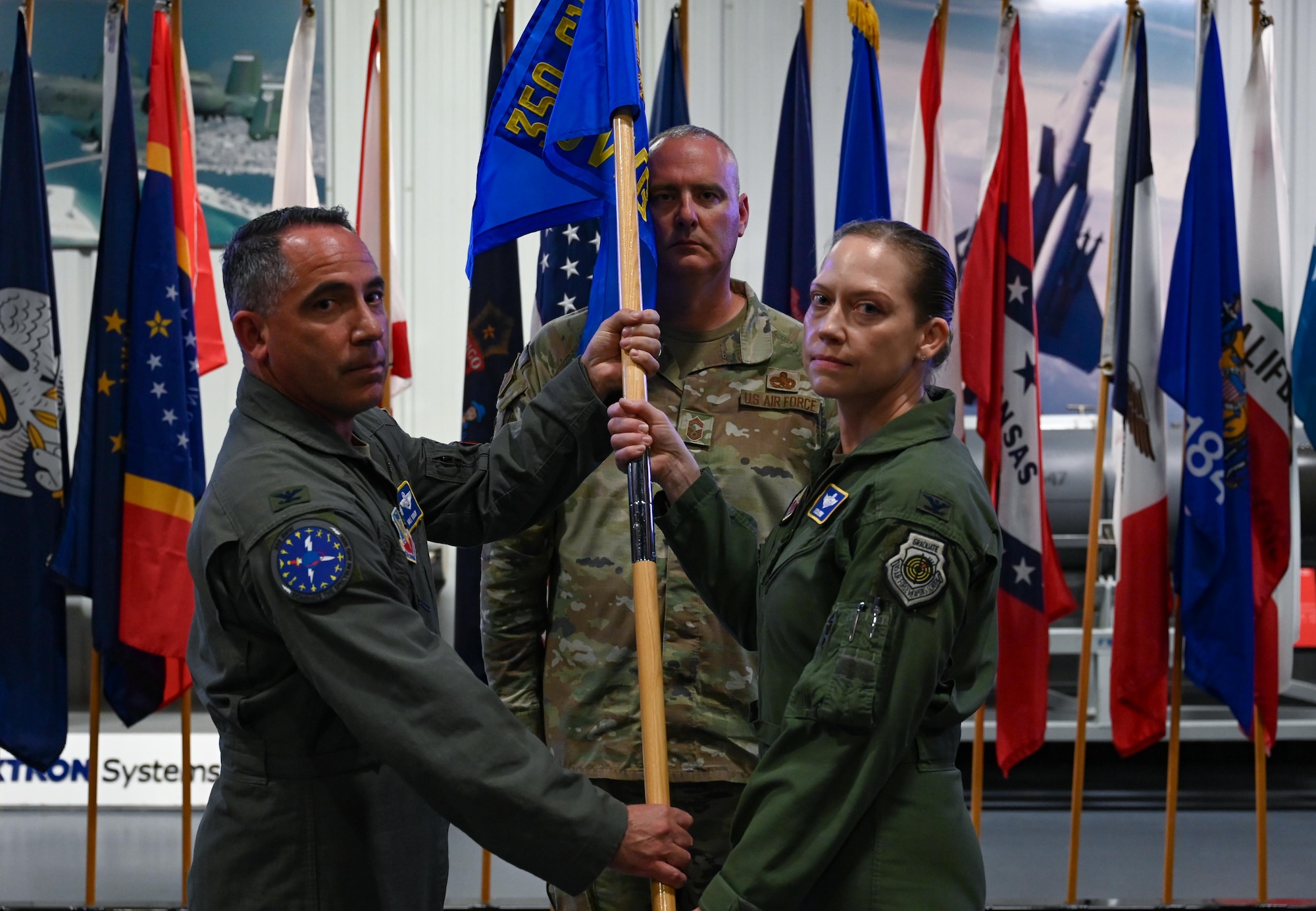 U.S. Air Force Col. Josh Koslov, 350th Spectrum Warfare Wing commander, left, passes the guidon to U.S. Air Force Col. Candice Sperry, 350th Spectrum Warfare Group commander, during a change of command ceremony at the U.S. Armament Museum, Eglin Air Force Base, Florida, June 7, 2024. The ceremony was the group’s first change of command in its history since activating in 2021. (U.S. Air Force photo by Capt. Benjamin Aronson)