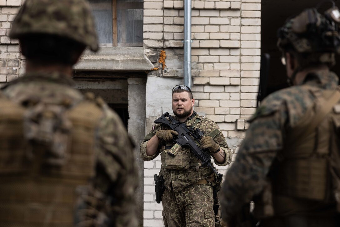A Latvian National Guard soldier with 4th Brigade, 44th Infantry Battalion, speaks to U.S. Marines with Battalion Landing Team 1/8, 24th Marine Expeditionary Unit Special Operations Capable, during military operations in urban terrain as part of Baltic Operations (BALTOPS) 24 in Skrunda, Latvia, June 8, 2024. BALTOPS 24 is the premier maritime-focused exercise in the Baltic Region. The exercise, led by U.S. Naval forces Europe-Africa and executed by Naval Striking and Support Forces NATO, provides a unique training opportunity to strengthen combined response capabilities critical to preserving freedom of navigation and security in the Baltic Sea. (U.S. Marine Corps photo by Cpl. Ryan Ramsammy)