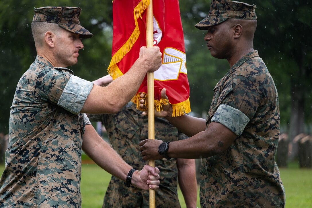 U.S. Marine Corps Lt. Col. Spencer D. Sweet, the incoming commanding officer of II Marine Expeditionary Force Support Battalion, left, receives the Marine Corps flag from Lt. Col. Brian M. Carthon, the outgoing commanding officer of II MSB, right, during the II MSB change of command ceremony at Marine Corps Base Camp Lejeune, North Carolina, June 10th, 2024. The change of command ceremony symbolizes the passing of authority and responsibility from the outgoing to the incoming commanding officer. (U.S. Marine Corps photo by Cpl. Noah Seal)