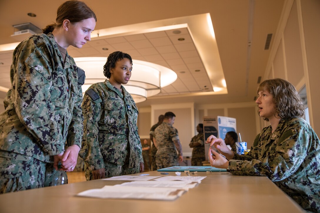 U.S. Navy Hospital Corpsman 2nd Class Elisabeth Basham, left, a command career counselor with the Naval Medical Readiness and Training command (NMRTC), and Hospital Corpsman 1st Class Tiara Monroe, center, a dental technician with NMRTC, learn about cardiovascular implants from Hospital Corpsman 1st Class Chessa Sheppard, right, a cardiovascular technician with Expeditionary Medical Facility Kilo during a Navy Career Fair at Marine Corps Base Camp Lejeune, North Carolina, June 6, 2024. The career fair, hosted by II Marine Expeditionary Force, served as a valuable platform for Sailors to increase awareness of diverse Navy career paths. (U.S. Marine Corps photo by Lance Cpl. Jack Labrador)