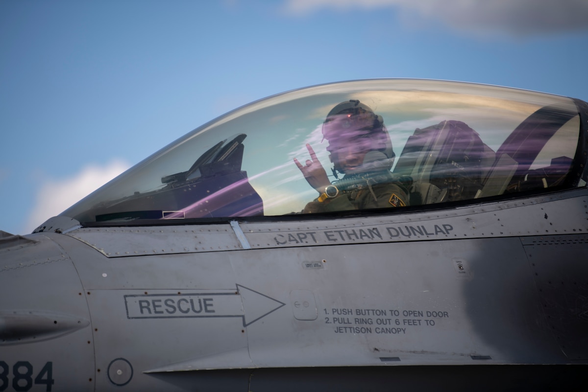 A pilot holds up a "rock on" hand signal while the cockpit of the plane is closed.