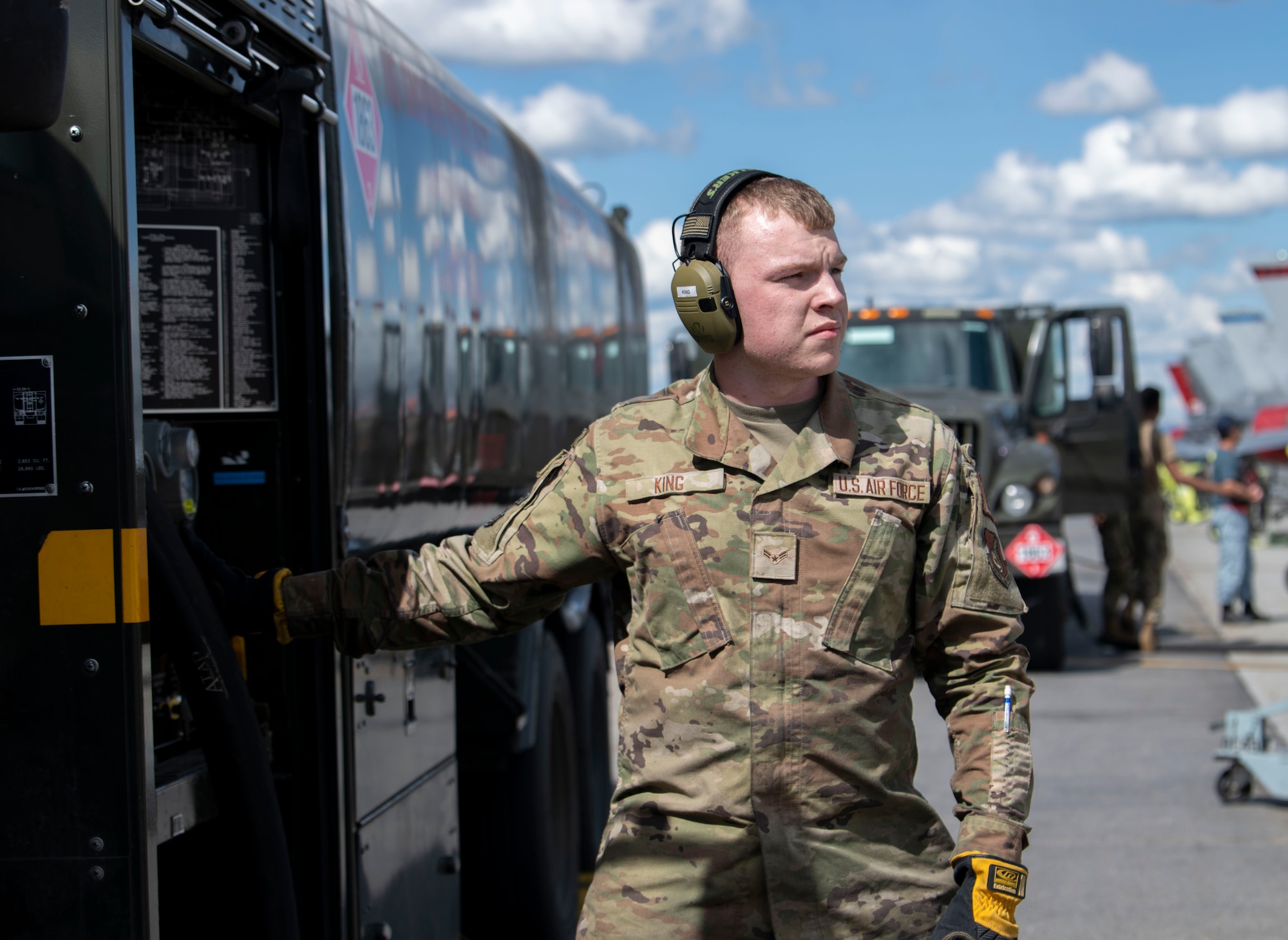 A maintainer hangs off the side of a fuel truck looking off to the side.