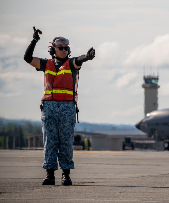 A maintainer signals a plane to move for by using is left arm to move back and forth and pointing his right arm out straight.