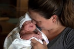 A woman in civilian attire holds a newborn baby.
