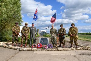 U.S. Air Force Lt. Col. Brad Fisher, commander of the 15th Airlift Squadron, and U.S. Air Force Maj. David Martin, commander of the 437th Aerial Port Squadron, stand with Ramsbury residents dressed as American World War II paratroopers in front of the memorial dedicated to the 437th Troop Carrier Group at RAF Ramsbury, June 8, 2024. The ceremony marked the 80th anniversary of D-Day, honoring the group's significant contributions during the invasion of Normandy and throughout World War II. (U.S. Air Force photo by 1st Lt. Taylor Ferry)