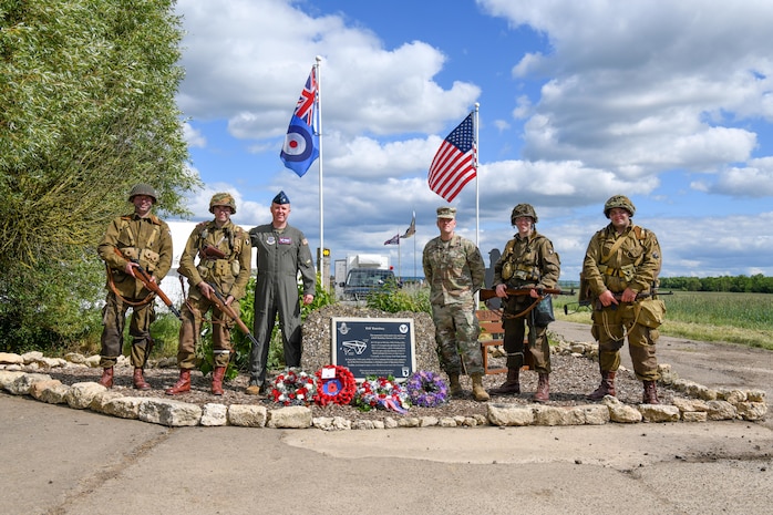 U.S. Air Force Lt. Col. Brad Fisher, commander of the 15th Airlift Squadron, and U.S. Air Force Maj. David Martin, commander of the 437th Aerial Port Squadron, stand with Ramsbury residents dressed as American World War II paratroopers in front of the memorial dedicated to the 437th Troop Carrier Group at RAF Ramsbury, June 8, 2024. The ceremony marked the 80th anniversary of D-Day, honoring the group's significant contributions during the invasion of Normandy and throughout World War II. (U.S. Air Force photo by 1st Lt. Taylor Ferry)