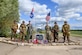 U.S. Air Force Lt. Col. Brad Fisher, commander of the 15th Airlift Squadron, and U.S. Air Force Maj. David Martin, commander of the 437th Aerial Port Squadron, stand with Ramsbury residents dressed as American World War II paratroopers in front of the memorial dedicated to the 437th Troop Carrier Group at RAF Ramsbury, June 8, 2024. The ceremony marked the 80th anniversary of D-Day, honoring the group's significant contributions during the invasion of Normandy and throughout World War II. (U.S. Air Force photo by 1st Lt. Taylor Ferry)