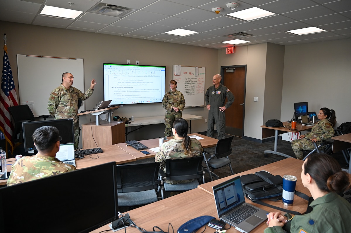 Master Sgt. William Bonner, center left, 433rd Airlift Wing Inspector General of Inspections and self-assessment program manager senior enlisted leader, briefs the accomplishments of Senior Master Sgt. Lisa Anderson, center, 26th Aerial Port Squadron SAPM, for her contribution to the IGI team to Col. William Gutermuth, center right, 433rd AW commander.