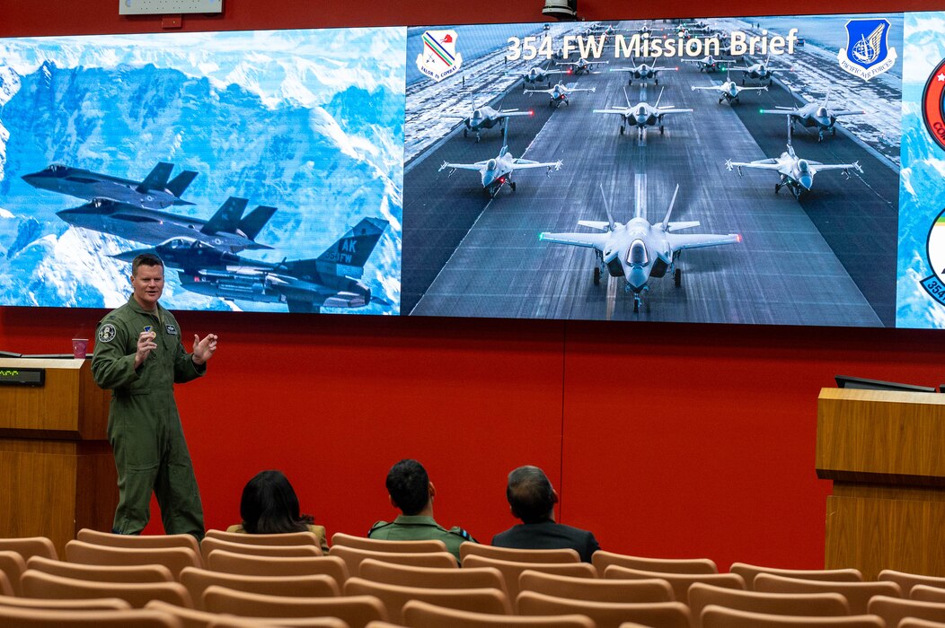 Col. Paul Townsend, 354th Fighter Wing commander stands in front of a powerpoint slide briefing 3 people.