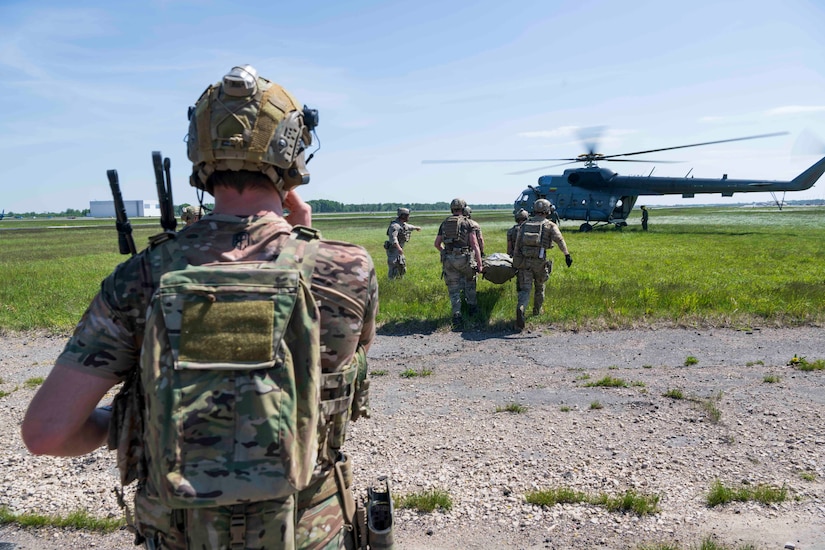 Sailors and Lithuania soldiers train near a helicopter in a field.