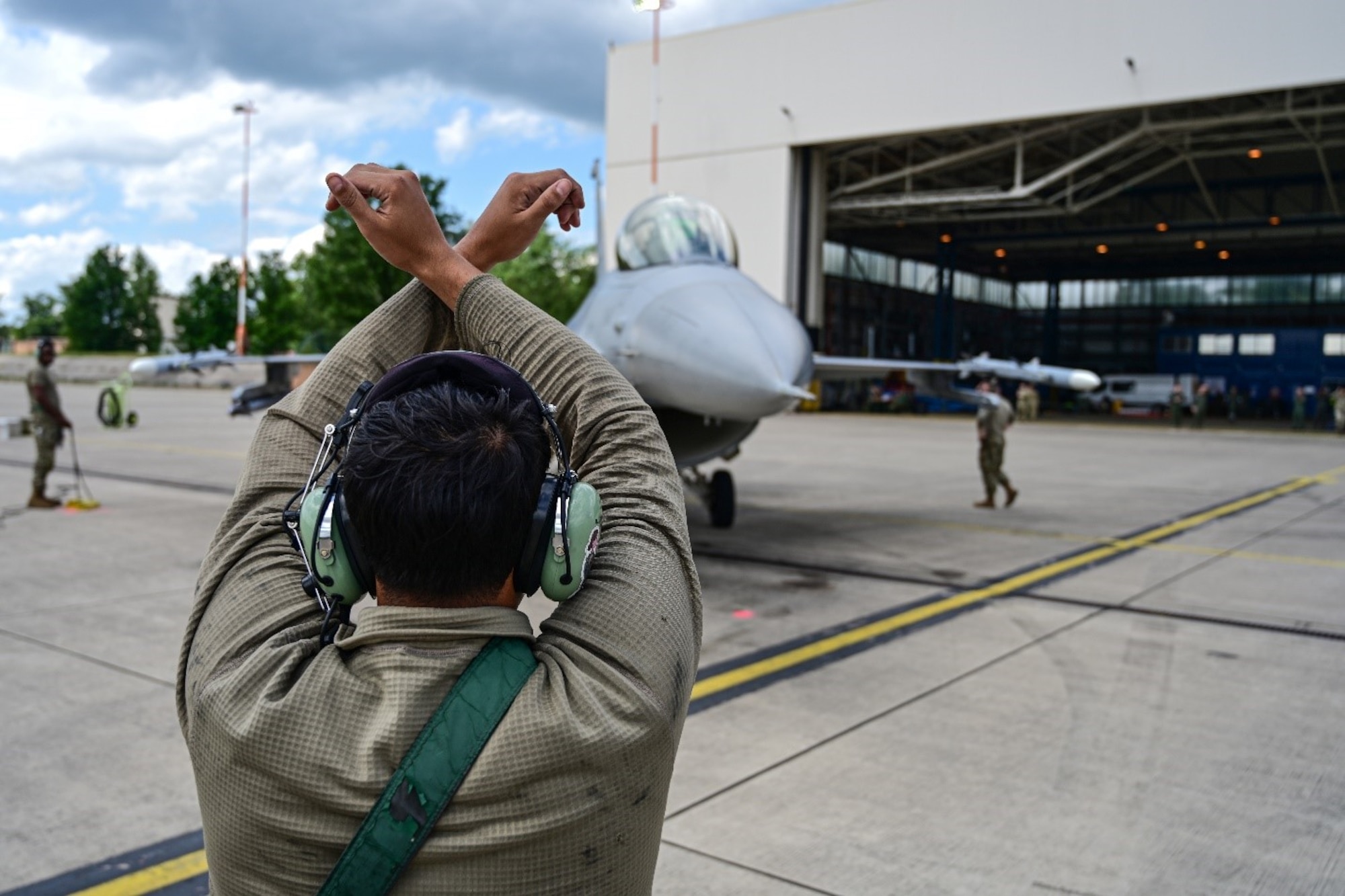 A U.S. Air Force Airman signals an F-16 Fighting Falcon to stop June 6, 2024, as part of a basic fighter maneuvers exercise held on Ramstein Air Base, Germany. The F-16 was an integral part of a simulated aerial combat exercise at the base which boasted a total of 37 aircraft, comprising both fourth and fifth-generation fighter jets. (U.S. Air Force photo by Senior Airman Christian Conrad)
