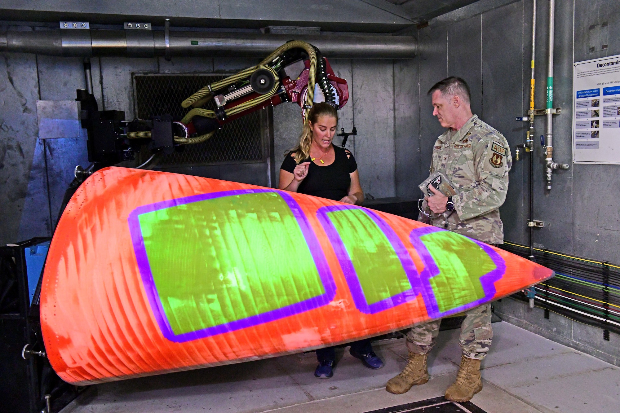 Two people stand behind an aircraft part while talking.