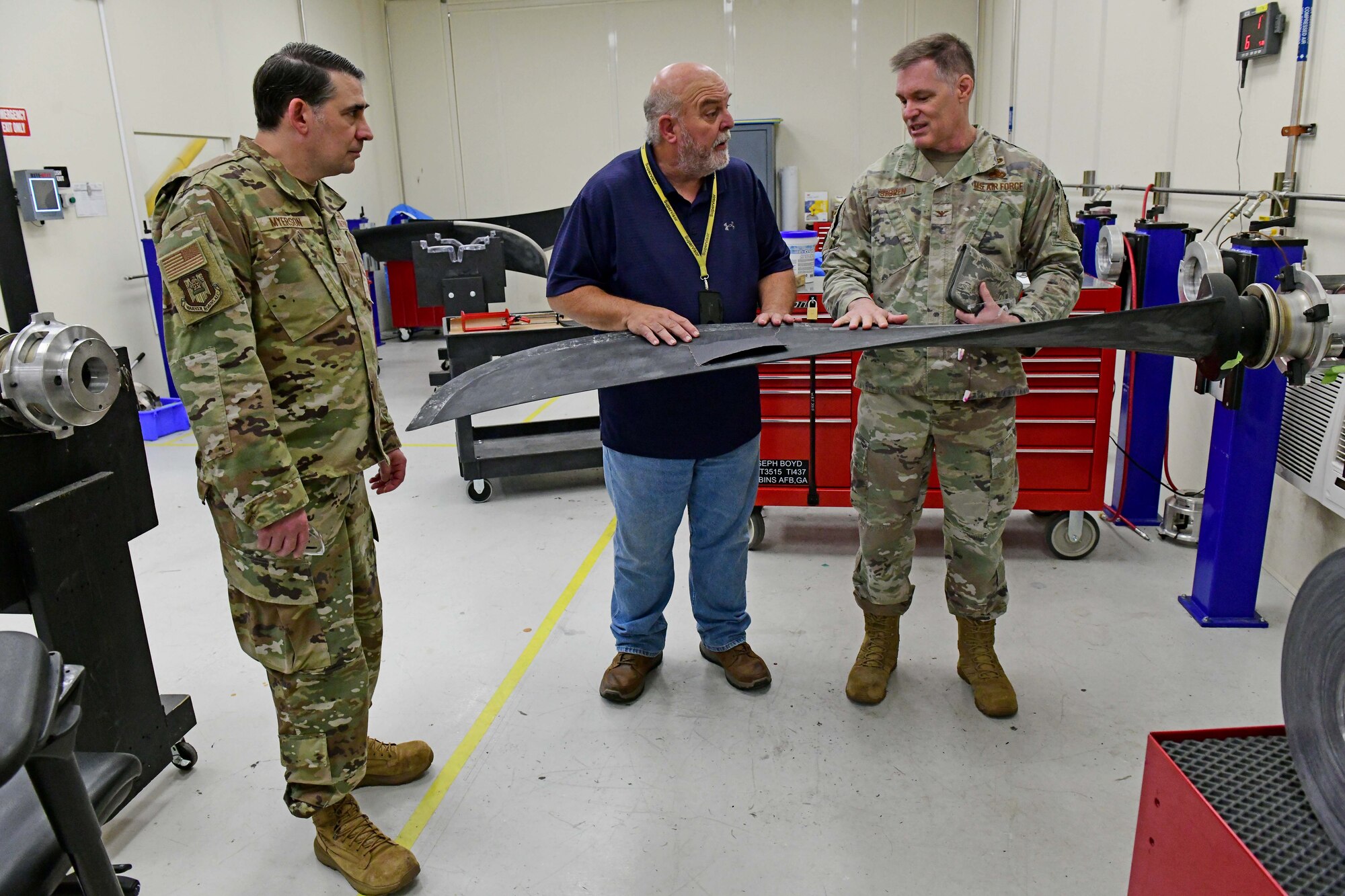 Three men are standing and talking while assessing an aircraft part.