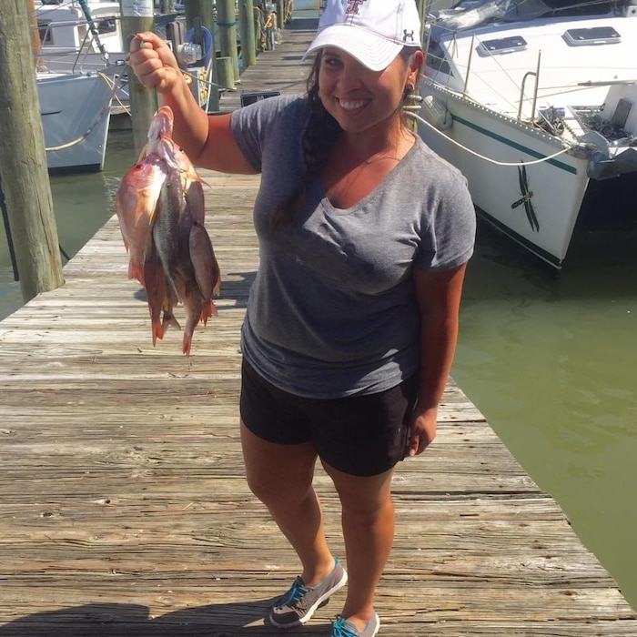 A woman is standing on a pier holding up several fish she caught.