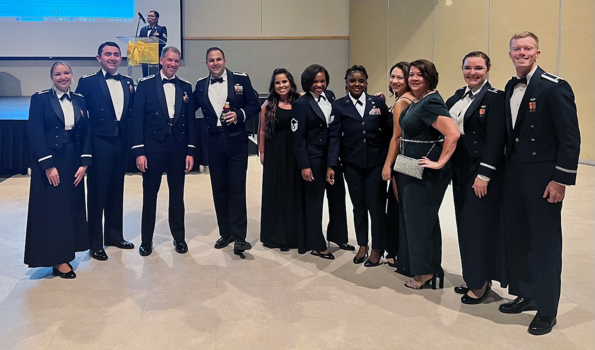 A group of military members and civilians are dressed in formal wear pose for a picture during an Air Force ball celebration.