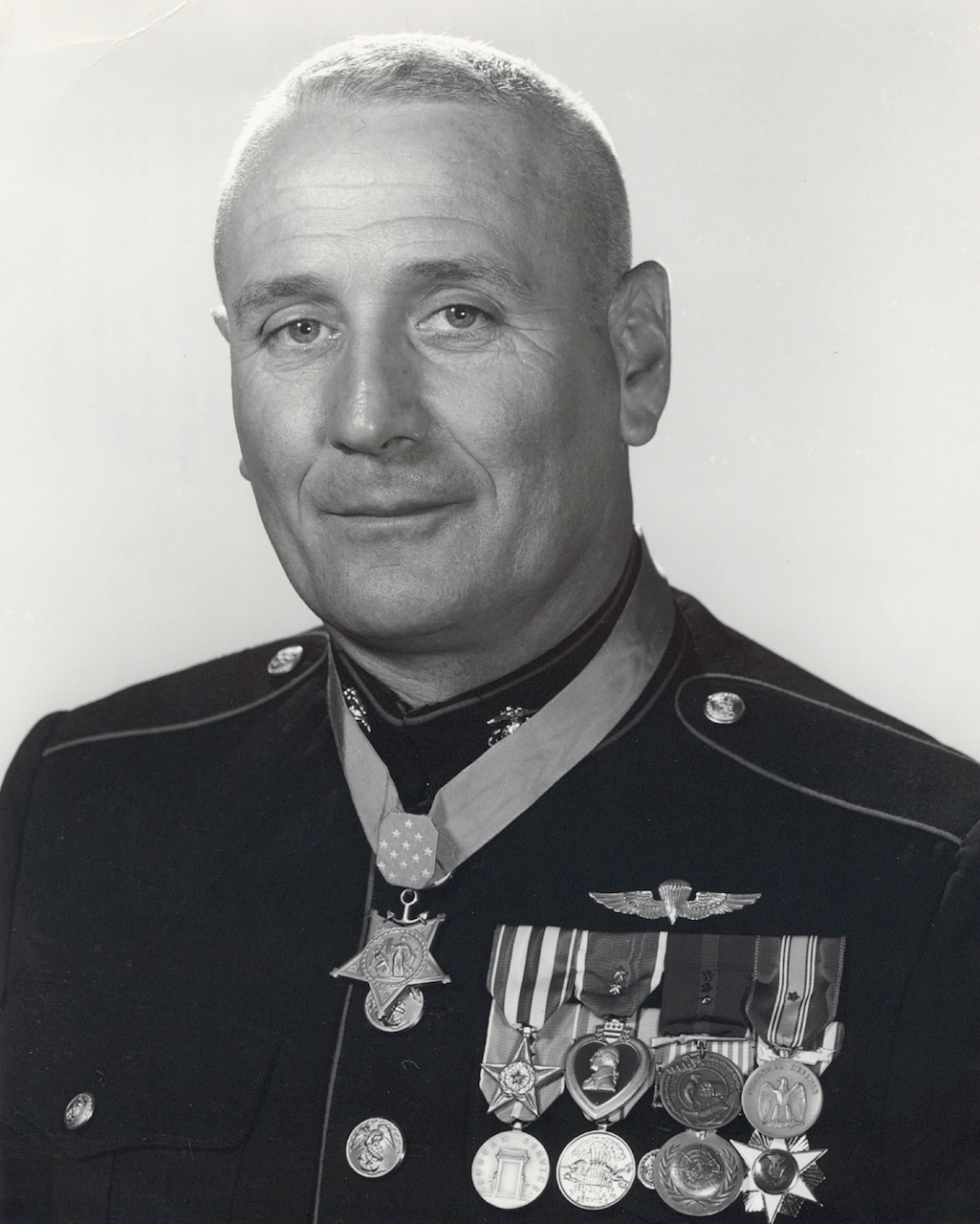 A man in dress uniform wears a medal around his neck and several more pinned to his lapel.