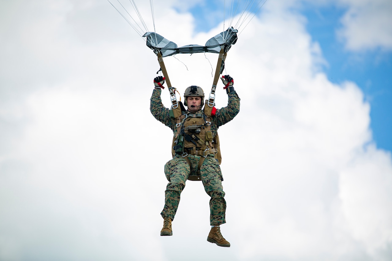 Close-up of a service member parachuting against a cloudy blue sky.