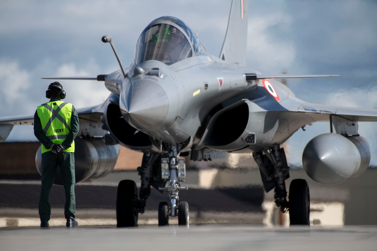 A maintainer from the Indian Air Force stands in front of a Rafale aircraft as the pilot conducts pre-checks.