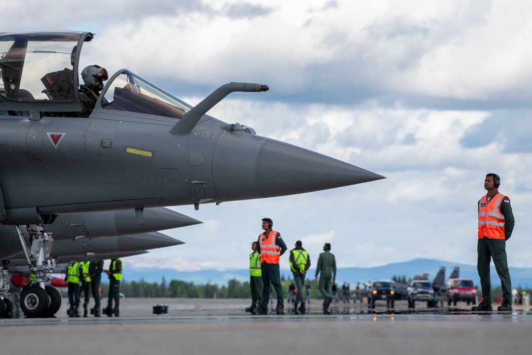 Rafale aircraft are lined up with Indian Air Force maintainers standing in front waiting to marshal the pilots and aircraft out for take-off.
