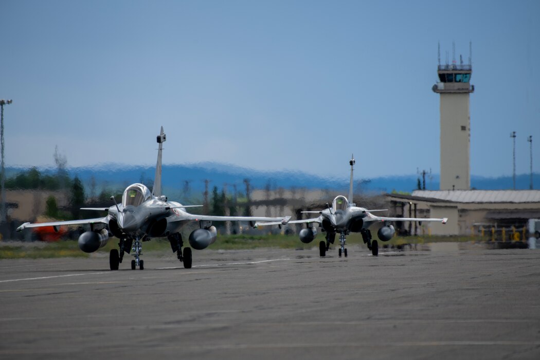 Two Rafale aircraft assigned to the Indian Air Force taxi down the flightline in a line with the Air Traffic Control Tower in the background.