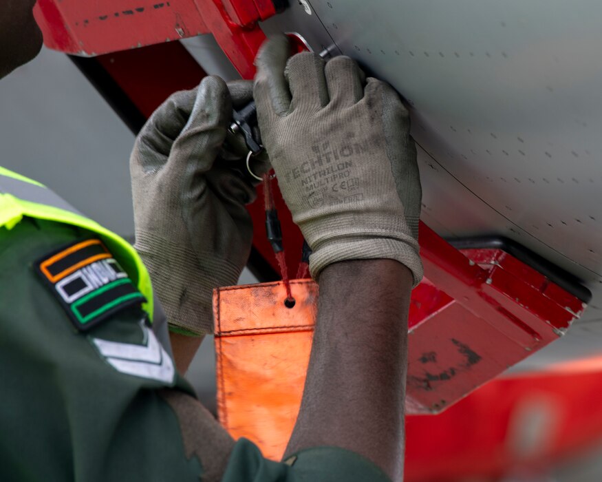 A close-up shot of the hands of a maintainer from the Indian Air Force. The maintainer is wearing grey maintenance gloves as he works on a Rafale aircraft.
