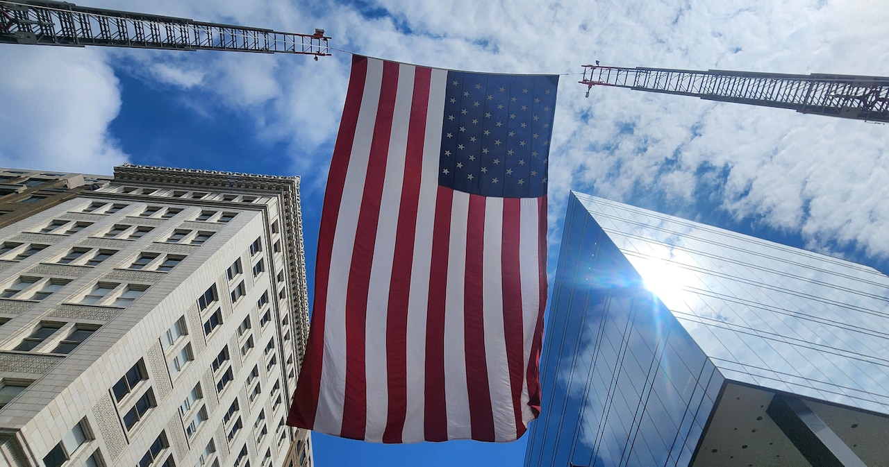 A flag is displayed above two building as seen from below.