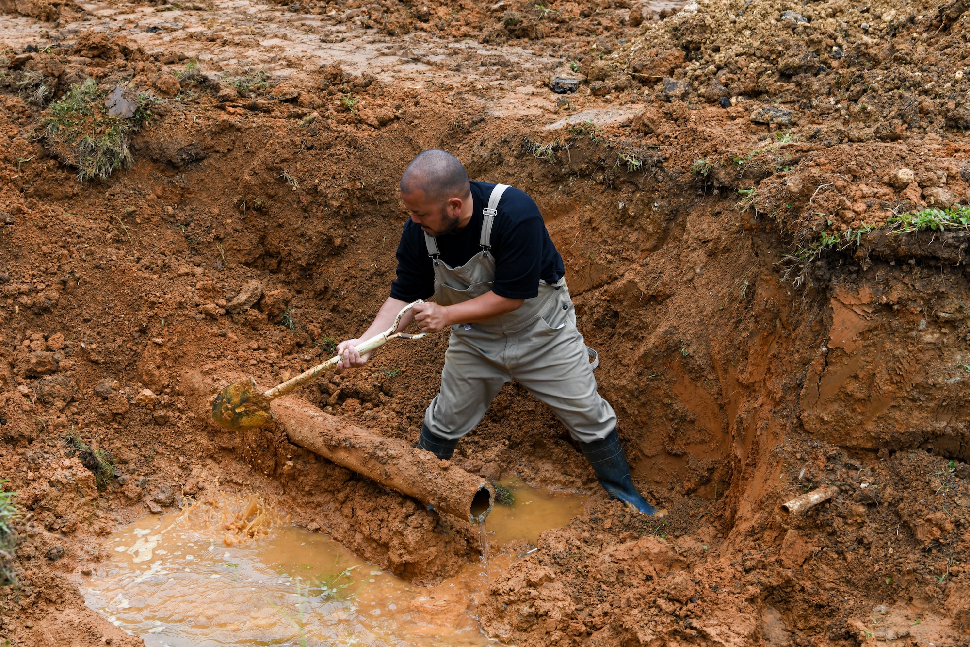 A Master Labor Contractor shovels mud and clay in a hole.