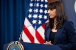 A person in business attire stands at a podium with a flag in the background.