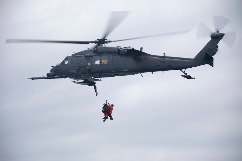 Two people dangle from a hovering helicopter mid air during training.