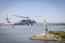 A helicopter flies near the Statue of Liberty with a city’s skyline in the background.