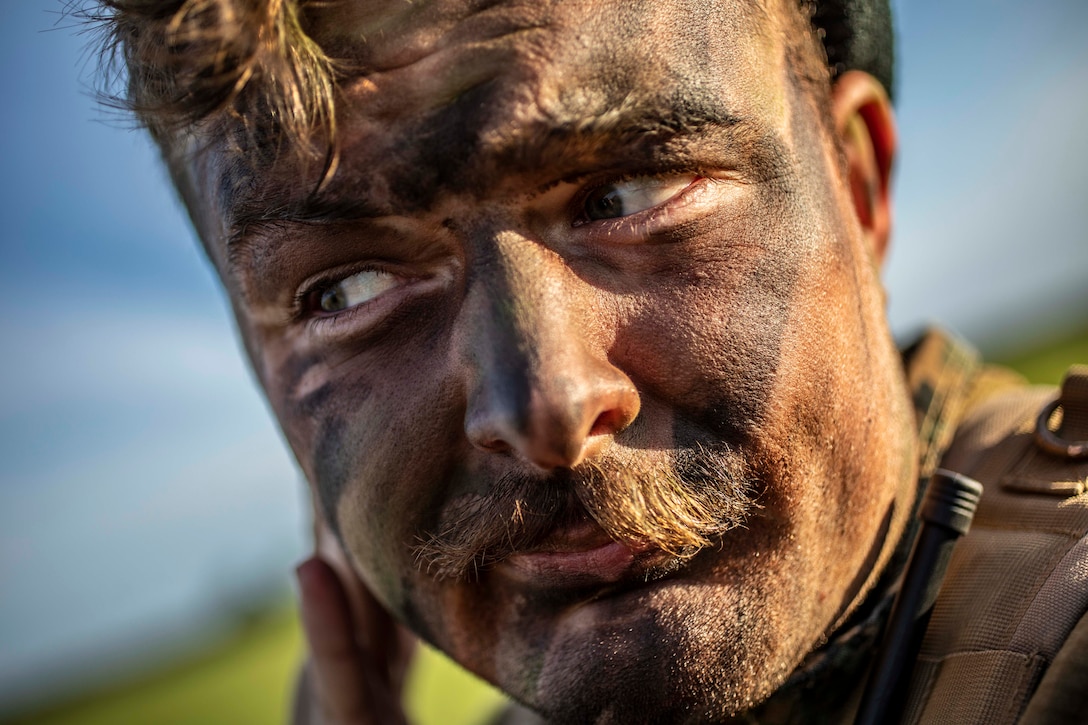 A Marine applies camouflage paint while looking away from the camera.