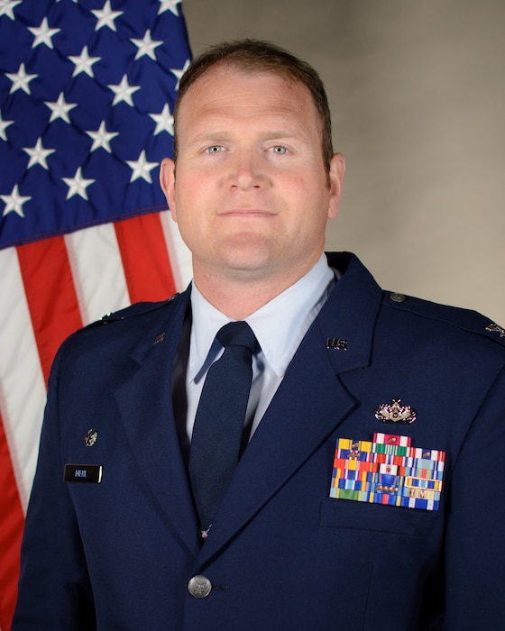 Service member smiles for official portrait in front of the US flag wearing their service dress blues