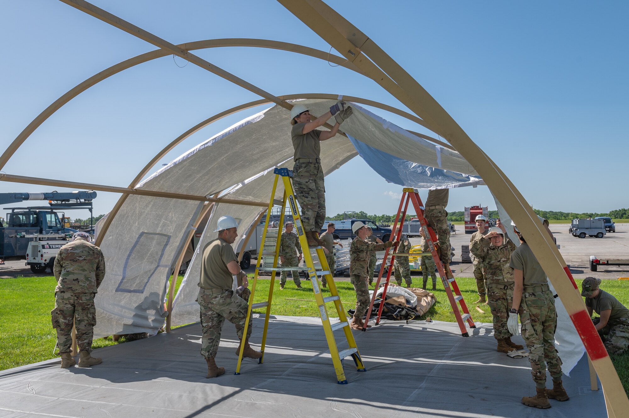 airmen work in the framework of a large tent some are on ladders and some hold the ladders in place