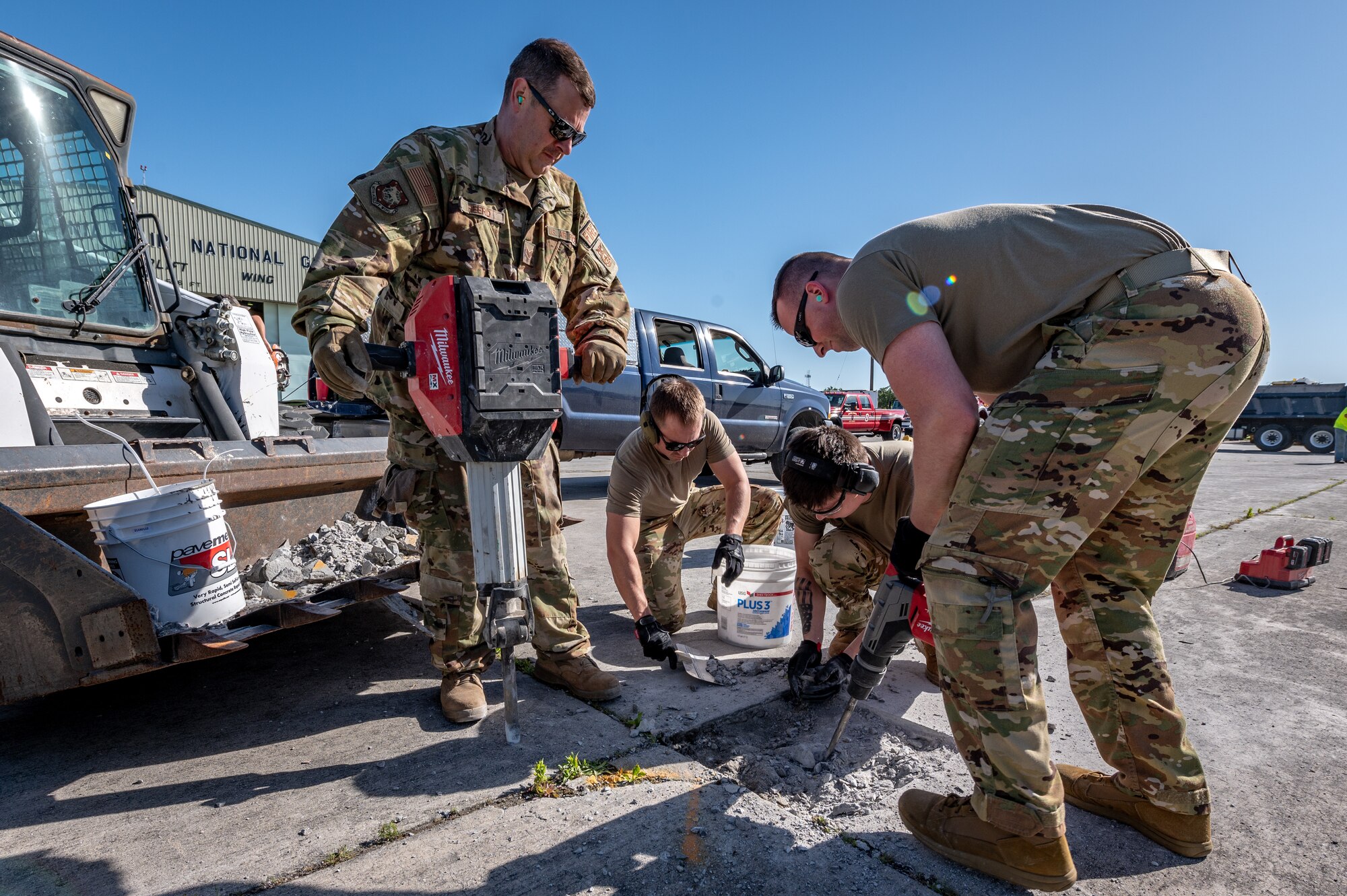 a man hold a jack hammer as three other men chip away concrete with small tools
