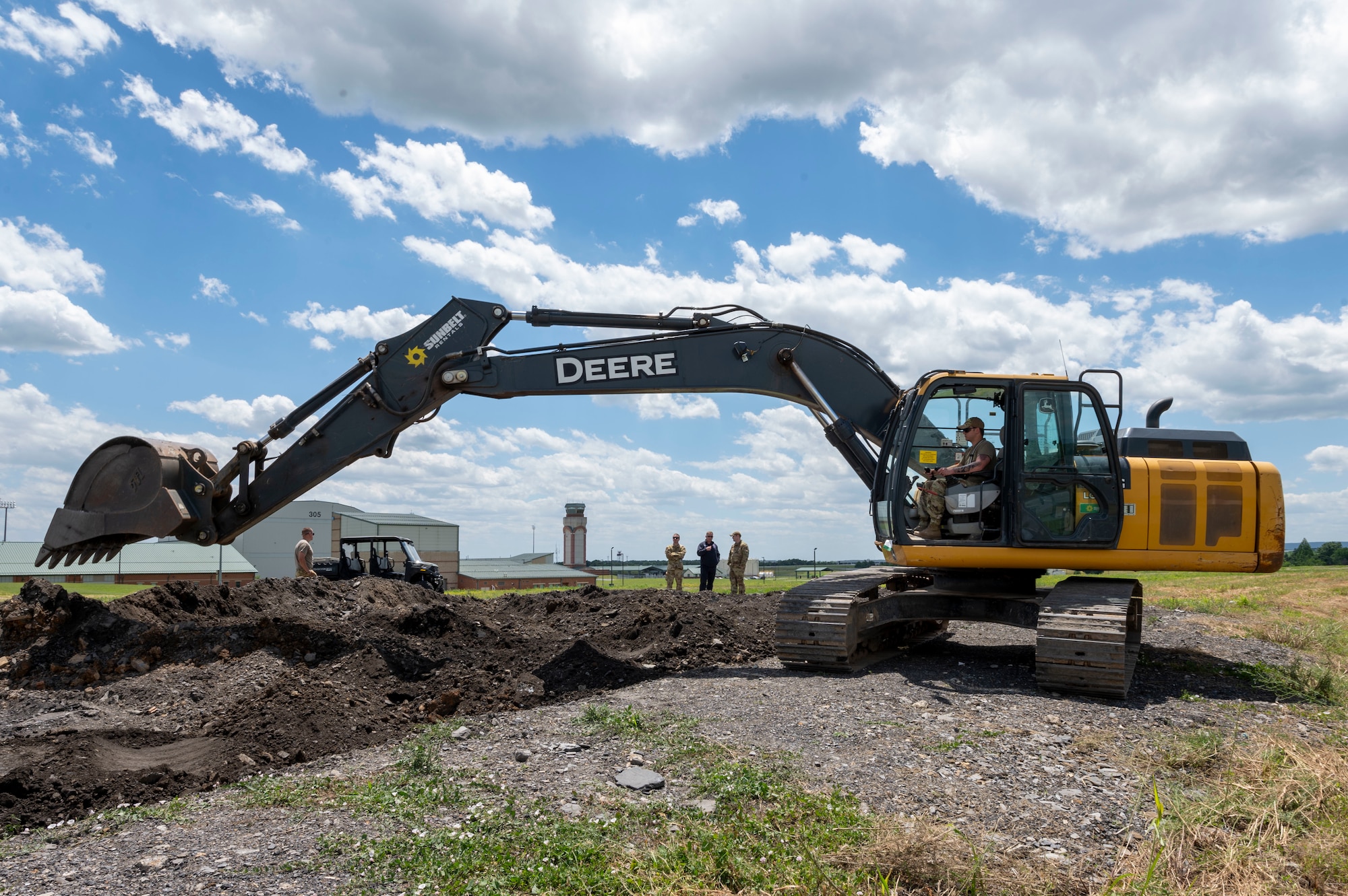 an excavtor moves dirt as people stand in the background watching