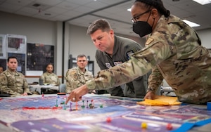 Major points to a point on a board game map while explaining to leadership what was learned during a Lead Wing Command and Control Course.