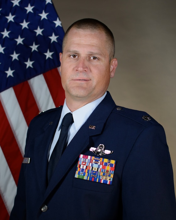 Service member poses for official portrait in front of the US flag wearing their service dress blues
