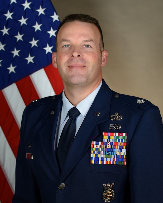 Service member smiles for official portrait in front of the US flag wearing their service dress blues