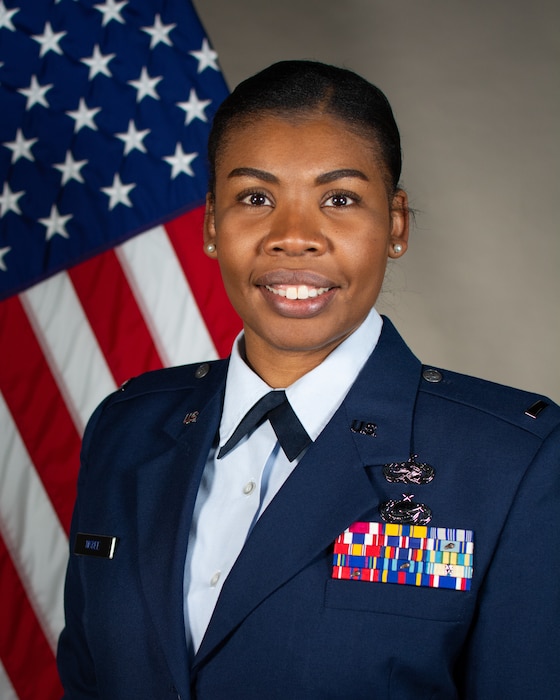 Service member smiles for official portrait in front of US flag wearing their service dress blues