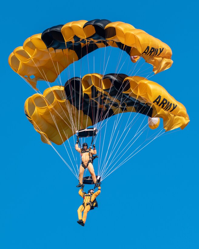 man wearing a parachute jump suit, flying with another person wearing a parachute jump suit, while parachuting.