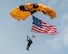 man wearing a parachute jump suit, flying the USA Flag while parachuting.