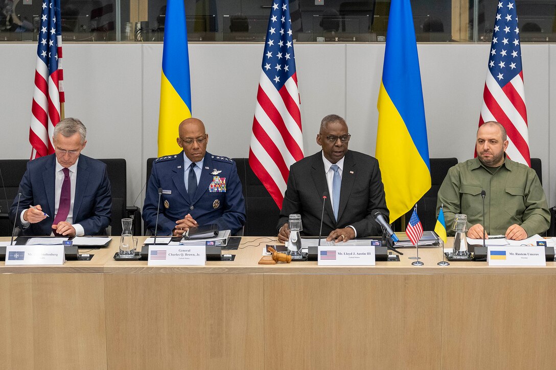 Secretary of Defense Lloyd J. Austin III sits at a long table with other officials, with U.S. and Ukrainian flags displayed behind them.