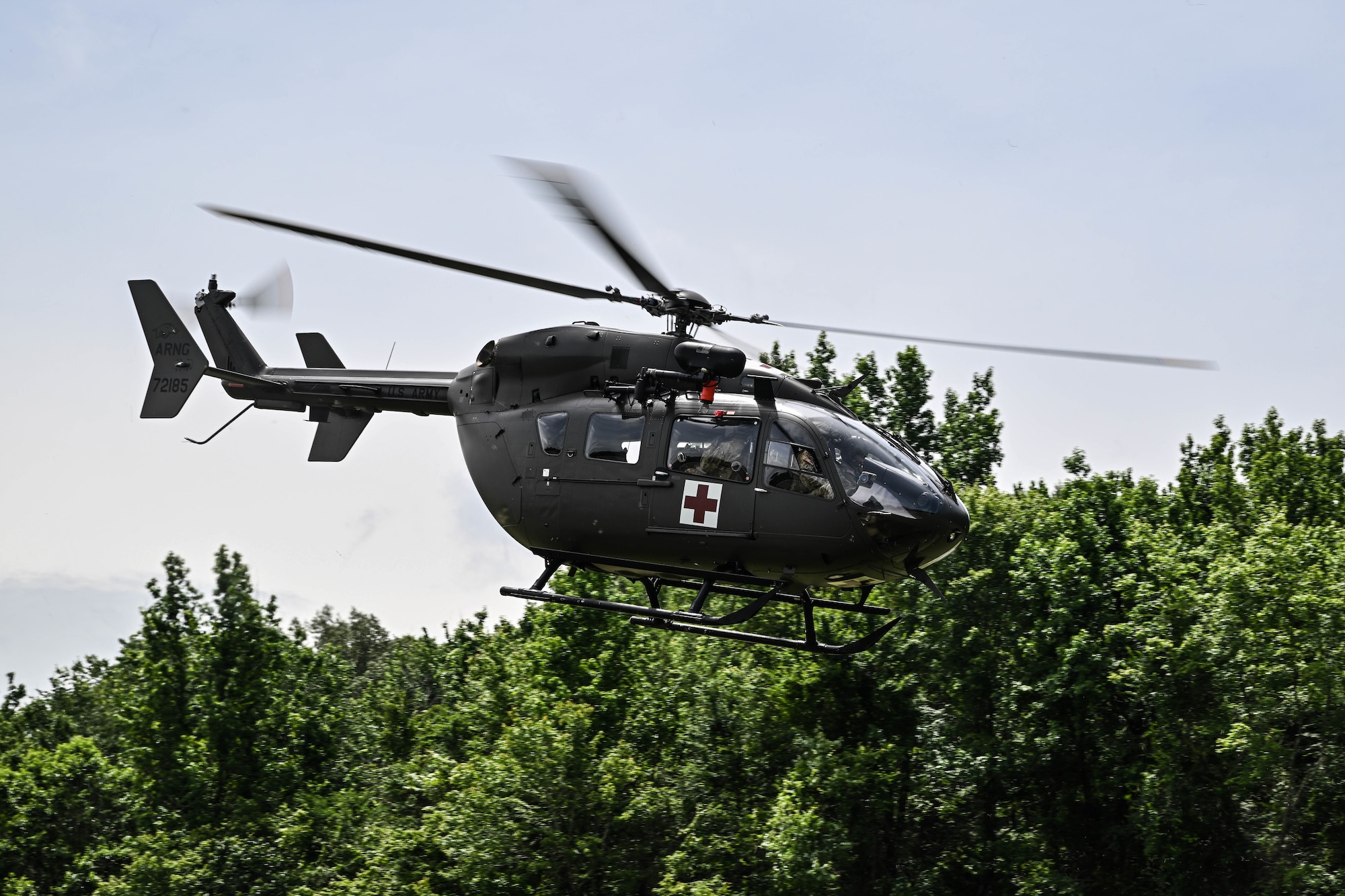 A helicopter flies by a tree line.