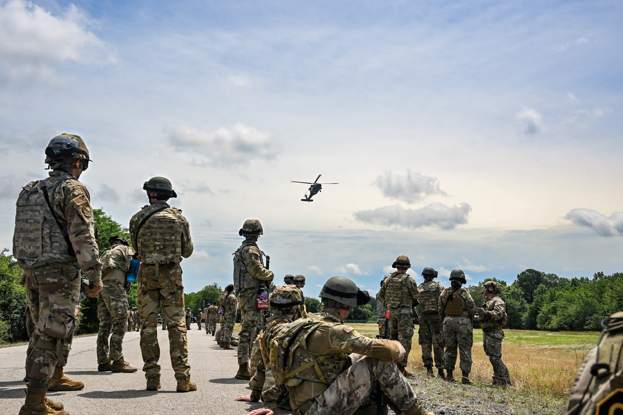 People in uniform look up at a helicopter.